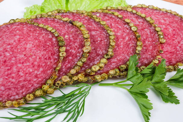 Plastry salami w skorup z pieprzu z zielonymi na danie zbliżenie - Zdjęcie, obraz