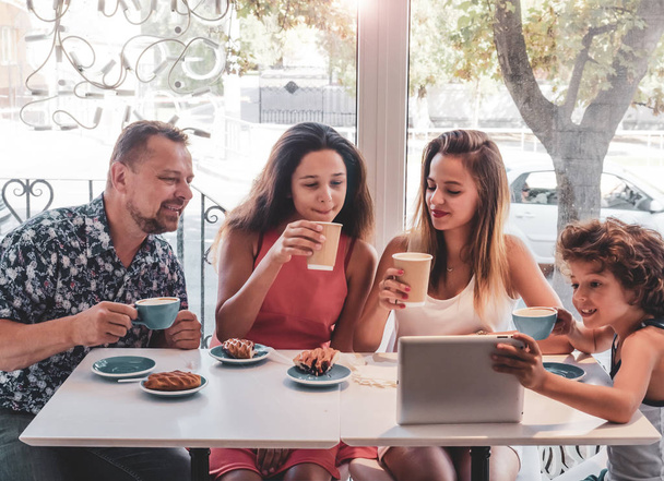 Gelukkige familie eten van ontbijt en het gebruik van Tablet PC. Een groot bedrijf met een digitaal tablet in café, glimlachend gelukkig man en zijn drie kinderen op zoek naar het scherm, met behulp van internet, online kopen - Foto, afbeelding