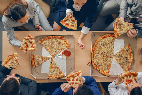 Top view of business people in formal wear sitting at table and having pizza for lunch. - Foto, Imagen