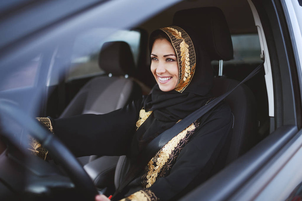 Gorgeous smiling muslim woman dressed in traditional wear driving her car. - Photo, Image