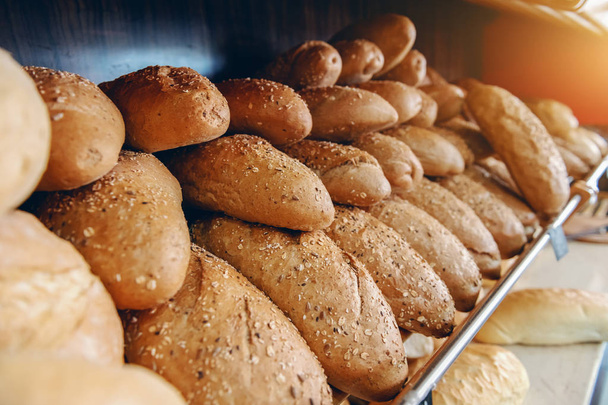 Frescos y deliciosos panes en fila en estantes listos para la venta. Interior de panadería
. - Foto, imagen