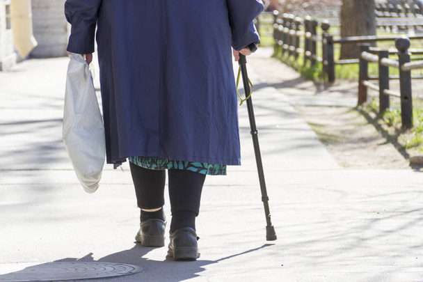 the elderly woman with a cane and a package walks on a square path - Foto, afbeelding