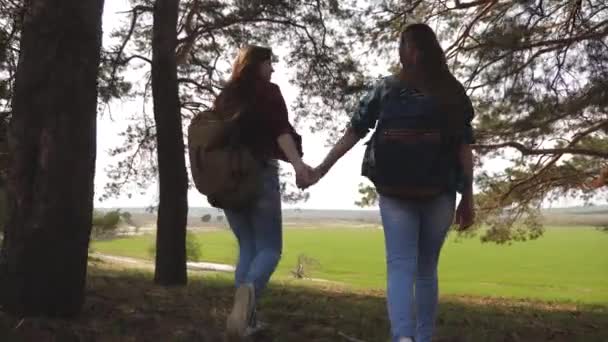 Women tourists go through forest. Sexy female travelers with backpacks straighten their arms to side, enjoying freedom. Girlfriends hold hands and laugh. Adventures in the campaign. Teamwork. - Footage, Video