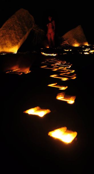 Μια γυναίκα στέκεται ανάμεσα σε δύο βράχους μπροστά σε ένα μονοπάτι φωτιάς σε μια πνευματική στιγμή. - Φωτογραφία, εικόνα