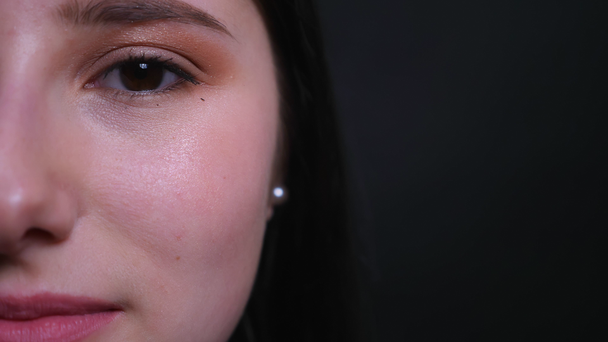 Closeup metade do rosto retrato de jovem atraente morena com maquiagem bonita olhando diretamente para a câmera com fundo isolado no preto
 - Filmagem, Vídeo