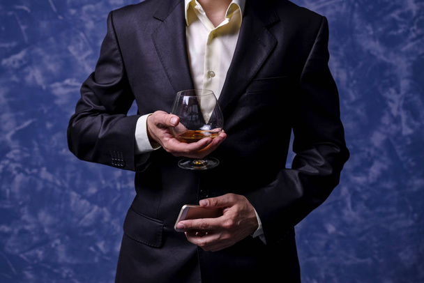 Business man with a glass of brandy and a smartphone. - Foto, afbeelding