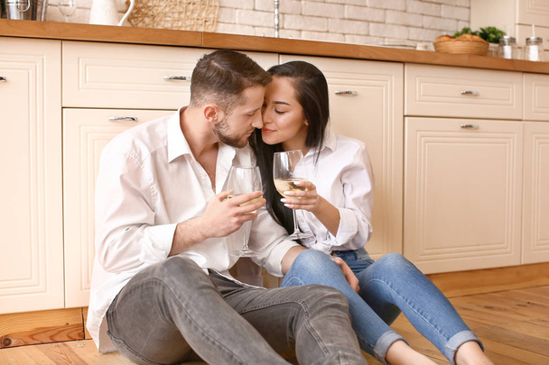Happy young couple drinking wine in kitchen - Foto, Bild