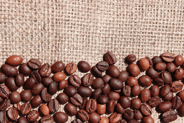 Ziarna kawy tło. Brown tekstury kawy. Ziarna kawy rozproszone na fakturze torby. - Zdjęcie, obraz