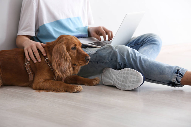 Nastoletni chłopiec z cute psa i laptopa siedzi w pobliżu światła ściany - Zdjęcie, obraz