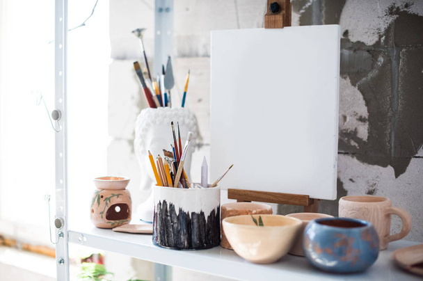 Lápices, lienzos y pinceles en estantería en estudio artístico
 - Foto, Imagen