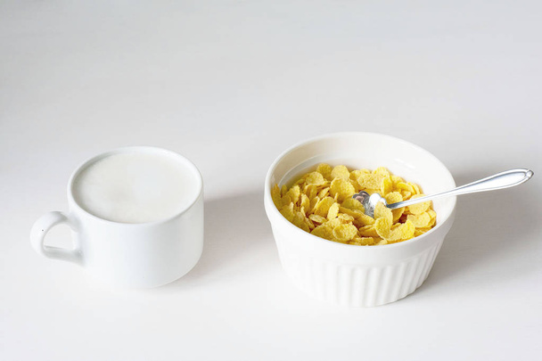 Desayuno saludable con copos de maíz y leche sobre fondo blanco
 - Foto, Imagen