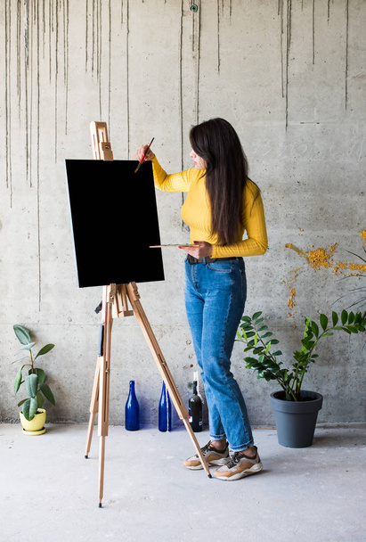 Jonge dame schilder kunstenaar met geïsoleerd canvas kunstwerk mock-up op ezel - Foto, afbeelding