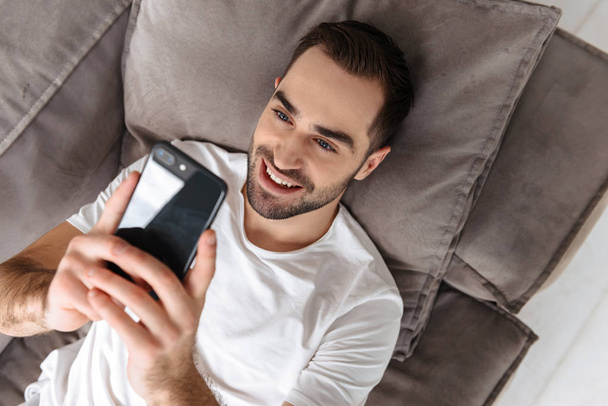 Photo of attractive guy holding and using smartphone while lying - Photo, Image