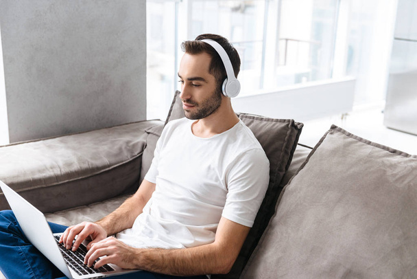 Photo of masculine guy in headphones holding and using silver la - Foto, afbeelding