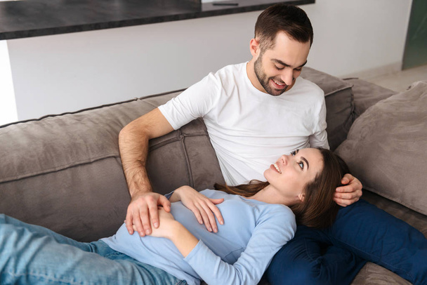 Happy young pregnant couple relaxing on a couch - 写真・画像