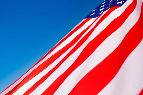 Американский флаг, летящий на ветру против голубого неба
 - Фото, изображение