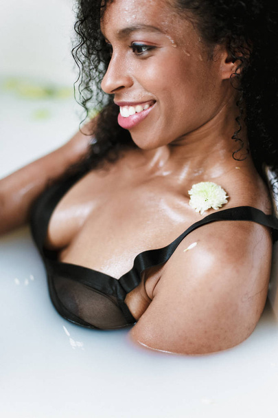 Foto de cerca de una chica negra tomando un baño con espuma, usando traje de baño. Concepto de spa y cuidado personal
. - Foto, imagen