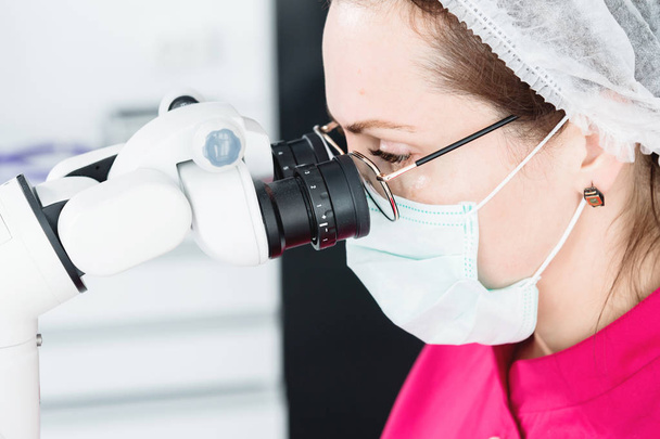 Close-up A woman in glasses with a professional dentist working with a professional stamotological microscope in her office. Stamotologist profession concept - Photo, image