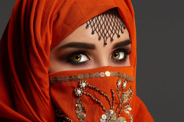 Estúdio tiro de uma jovem mulher encantadora vestindo o hijab terracota decorado com lantejoulas e jóias. Estilo árabe
. - Foto, Imagem