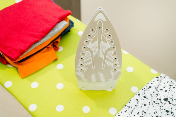 Modern electric iron and pile of clothes on ironing board - Photo, image