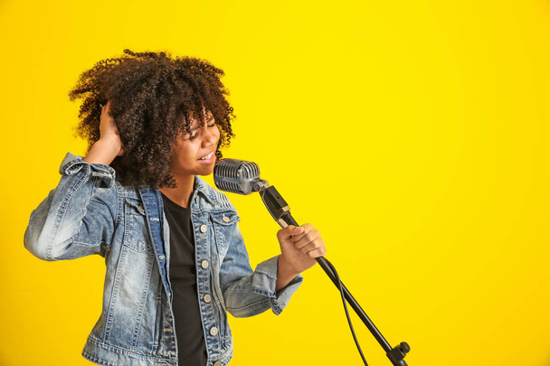 Menina afro-americana com microfone cantando contra fundo de cor
 - Foto, Imagem