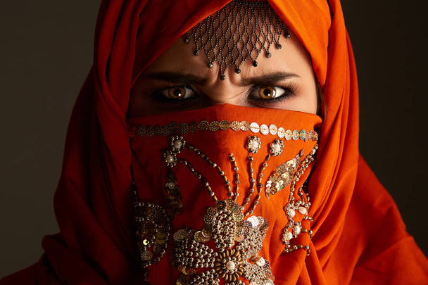 Foto de estudio de una joven encantadora mujer con el hiyab de terracota decorado con lentejuelas y joyas. Estilo árabe
. - Foto, Imagen