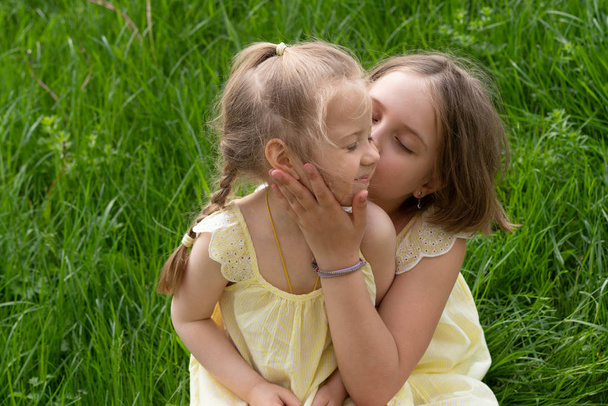 two girls sit on green grass in yellow dresses - Photo, Image