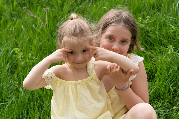 dos niñas se sientan en la hierba verde en vestidos amarillos
 - Foto, imagen
