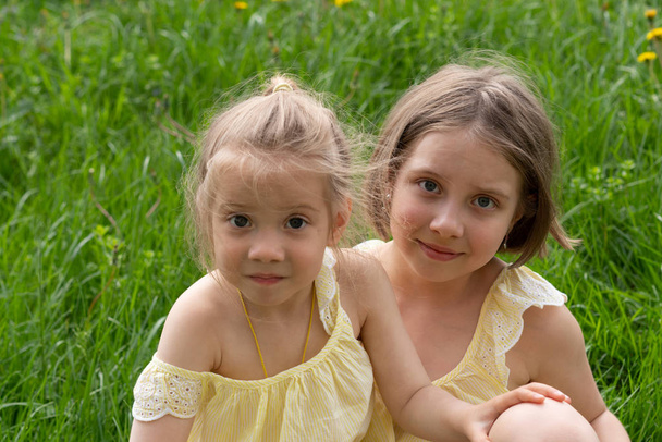 dvě dívky sedí na zelené trávě ve žlutých šatech - Fotografie, Obrázek