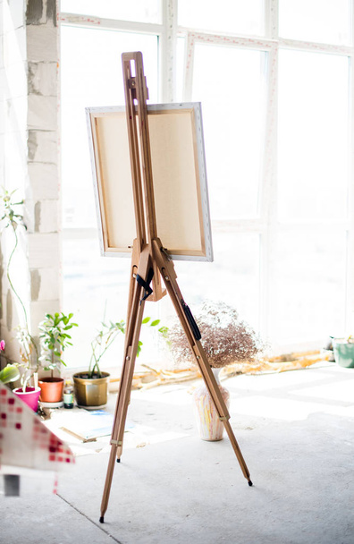 Easel with canvas standing in empty artistic studio - Fotoğraf, Görsel