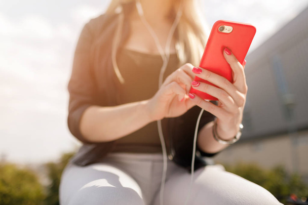 Młoda stylowa piękna dziewczyna słuchając muzyki w słuchawkach. Dziewczyna za pomocą smartfona i słuchawek, słuchać muzyki, park, outdoor. - Zdjęcie, obraz