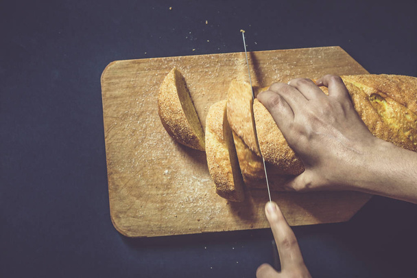Food concept. Hand cutting bread. Slicing a bread. Top view. - 写真・画像