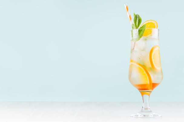 Fresh orange cocktail with slices fruits, mint, straw, ice cubes in misted glass on white wood table and blue color wall, copy space. - Foto, Imagem
