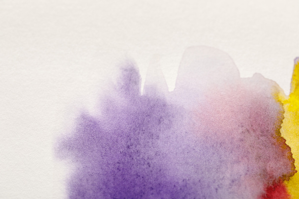 close up view of yellow, purple and red watercolor paint spills on white background - Zdjęcie, obraz