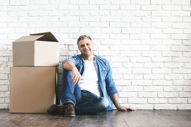 Handsome mature man with moving boxes near white brick wall - Photo, Image