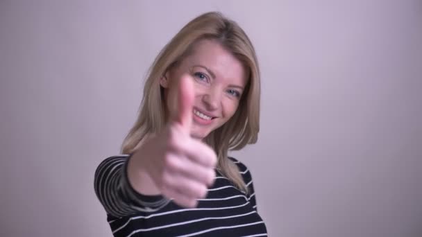 Крупним планом портрет дорослої привабливої блондинки білої жінки, що показує великий палець вгору посміхаючись дивитися на камеру з фоном ізольовані на білому
 - Кадри, відео