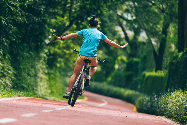 Woman riding a bike on sunny park trail with no-hands - Фото, зображення