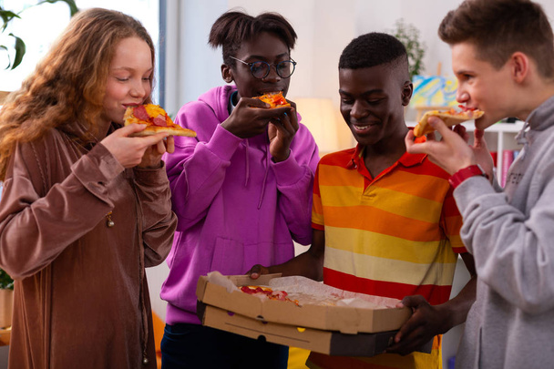 Four stylish teenagers eating delicious pizza after school - Foto, Imagem