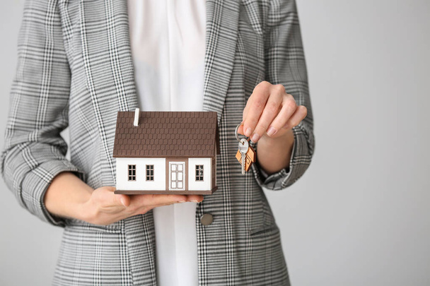 Женщина-агент по недвижимости с моделью дома и ключом на сером фоне, крупный план
 - Фото, изображение