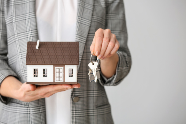 Immobilienmaklerin mit Hausmodell und Schlüssel auf grauem Hintergrund, Nahaufnahme - Foto, Bild
