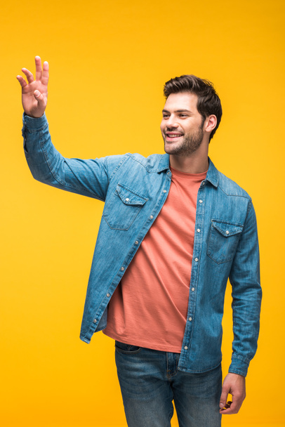 handsome man gesturing with hand and smiling isolated on yellow - Fotografie, Obrázek