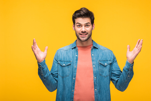 confused handsome man gesturing with hands and looking at camera isolated on yellow - 写真・画像