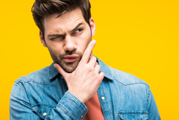 hombre guapo confundido tocando la barbilla aislado en amarillo
 - Foto, Imagen