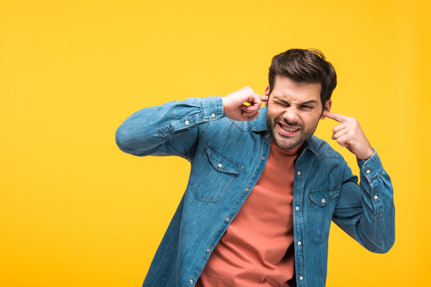 dissatisfied handsome man plugging ears with fingers isolated on yellow - Fotoğraf, Görsel