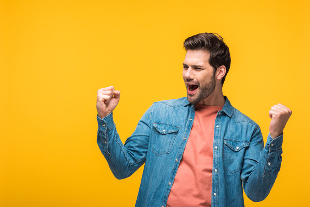 happy handsome man cheering with clenched fists isolated on yellow - Foto, Bild