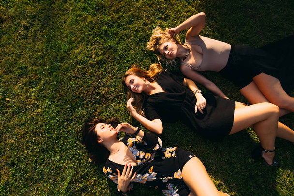 dziewczyny w pięknych sukienkach leżą na trawie i uśmiechem. Widok z góry - Zdjęcie, obraz