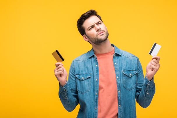 confundido hombre guapo sosteniendo tarjetas de crédito aisladas en amarillo
 - Foto, Imagen