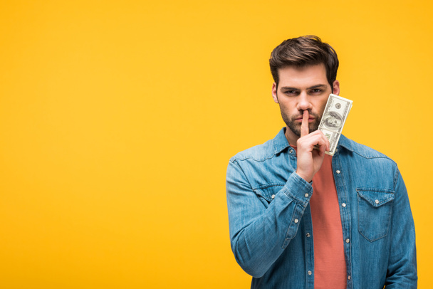 handsome man doing silence gesture and holding money isolated on yellow - Photo, Image