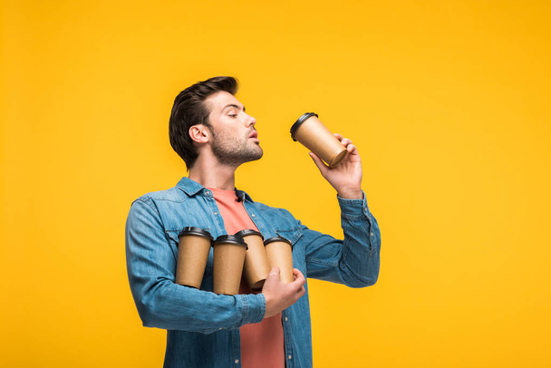 handsome man holding paper cups with coffee to go isolated on yellow - Photo, Image