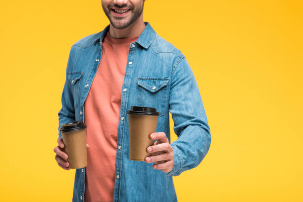 Vista cortada de homem sorridente segurando café para ir isolado no amarelo
 - Foto, Imagem
